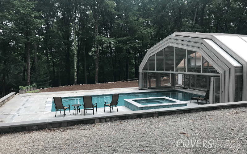 Side exterior view of opened residential pool dome in backyard forest in Kinnelon