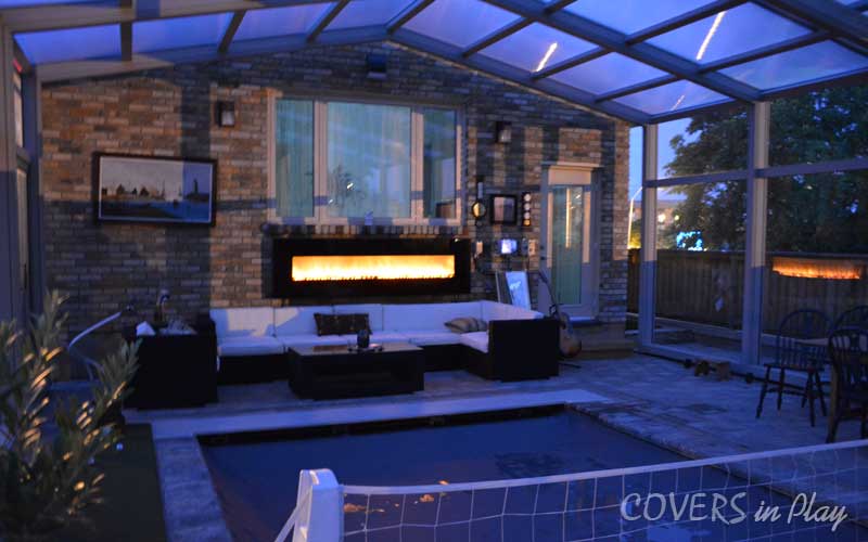 Interior view of closed pool enclosure at night with glowing fireplace in Burlington